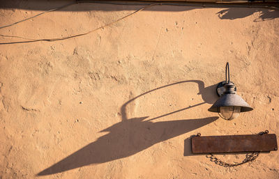 Low angle view of lamp with shadow on wall during sunny day