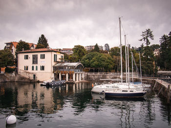 Sailboats moored on river by building against sky