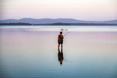 Rear view of woman fishing in lake during sunset