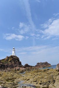 Lighthouse on rock by building against sky