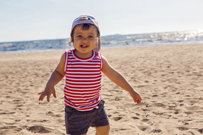 Child in a t-shirt and shorts walks on the beach near the sea