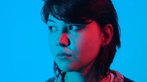 Close-up of woman looking away against blue background