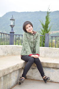 Portrait of a smiling young woman sitting on retaining wall