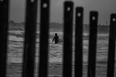 Surfer walking at beach seen through wooden posts