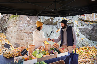 Smiling woman holding credit card reader for male customer at market stall