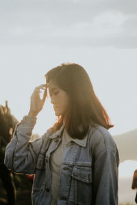 Woman looking down while standing against sky