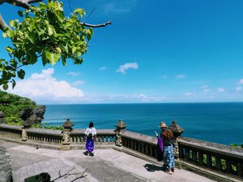 Women walking on promenade at beach against blue sky