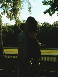 Rear view of couple kissing against trees in city