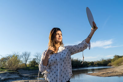 Young woman standing by water against clear sky