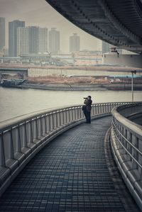 Man standing on bridge over river in city