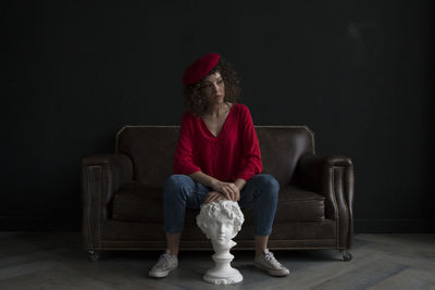 Portrait of woman sitting on sofa against wall