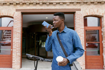 Young man using mobile phone while standing against building
