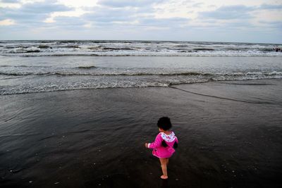 Rear view of girl standing on beach against sky