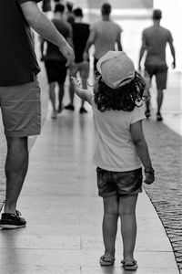 Rear view of girl with father standing on footpath