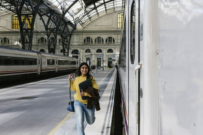 Smiling woman with laptop bag running on platform to catch train