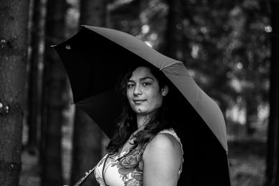 Portrait of smiling young woman with umbrella standing in forest