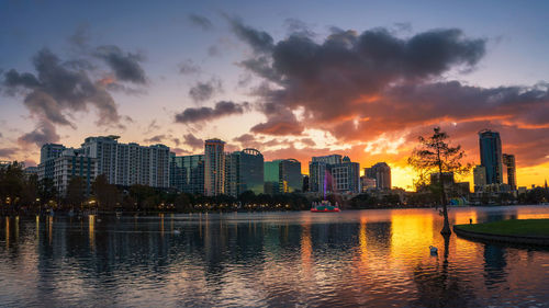 River by buildings against sky during sunset