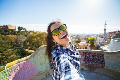 Portrait of smiling young woman in city against sky