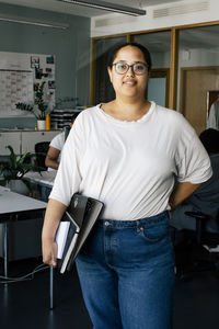 Portrait of female computer programmer holding files while standing at office