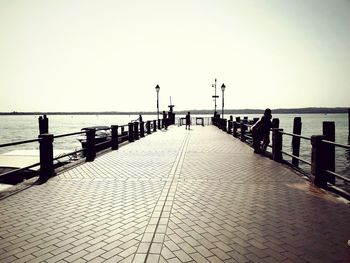 People on pier by sea against clear sky