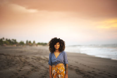 Woman standing at beach against sky during sunset