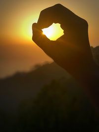 Close-up of silhouette hand against sky during sunset