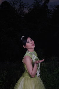 Smiling young woman wearing green dress and tiara while standing at night