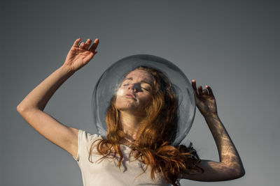 Low angle view of young woman wearing glass helmet in head against gray background