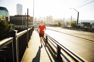 Full length of man jogging on footpath in city during sunny day