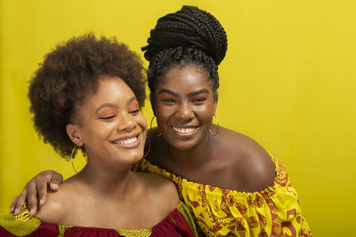 Portrait of two women against yellow background. they wear yellow and red colored clothes.