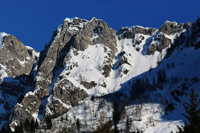 Low angle view of snowcapped mountains against clear blue sky