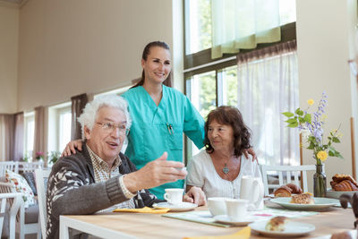 Smiling healthcare worker and senior woman listening to man during breakfast at home
