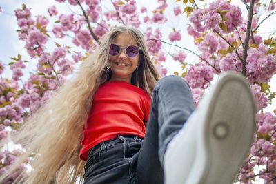 Low angle view of young woman wearing sunglasses standing against trees