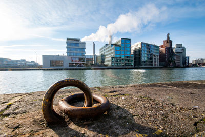 Metal structure by river against buildings in city against sky