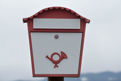 A white european mailbox with post horn and a red frame