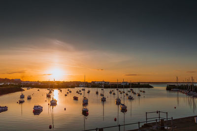 Boats moored in harbor at sunset