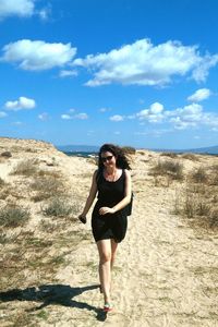 Portrait of smiling young woman standing on desert against sky