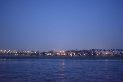 Illuminated city by sea against clear blue sky at night