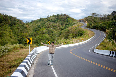 Full length of man with arms outstretched standing on country road