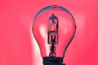 Close-up of illuminated light bulb against pink background