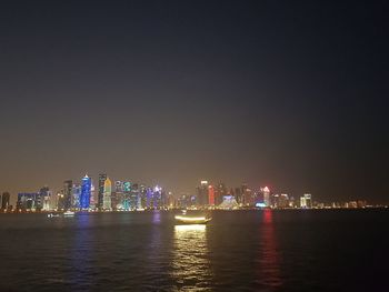 Illuminated buildings by sea against sky at night