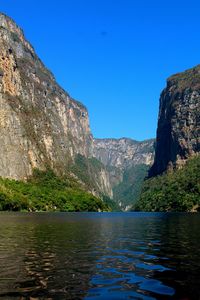 Scenic view of river by mountains against clear blue sky