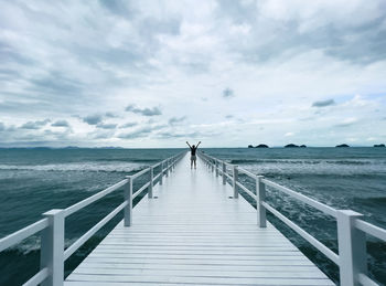 Adult standing on pier facing blue sea