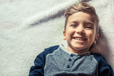High angle portrait of cute smiling boy lying on bed at home
