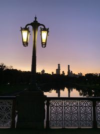 Illuminated street light by building against sky at dusk