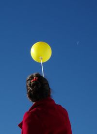 Low angle view of woman holding balloon while standing against sky