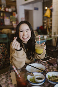 Happy woman gesturing while holding drink at restaurant