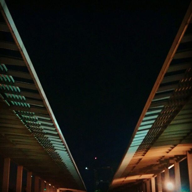 low angle view, architecture, built structure, illuminated, night, ceiling, clear sky, building exterior, lighting equipment, building, railing, copy space, indoors, no people, connection, sky, bridge - man made structure, modern, light - natural phenomenon