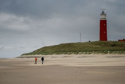 Lighthouse on beach by sea against sky