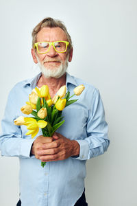 Portrait of senior man holding flowers against white background